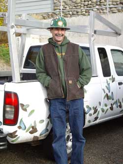 Blaine Rowland stands behind his truck. He's wearing a hard hat and his truck has leaves painted on it.