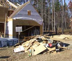 House under construction with lots of wood, drywall, and other debris piled in front.