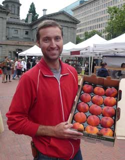 Photo of Jaret at the farmer's market holding a box of peaches.