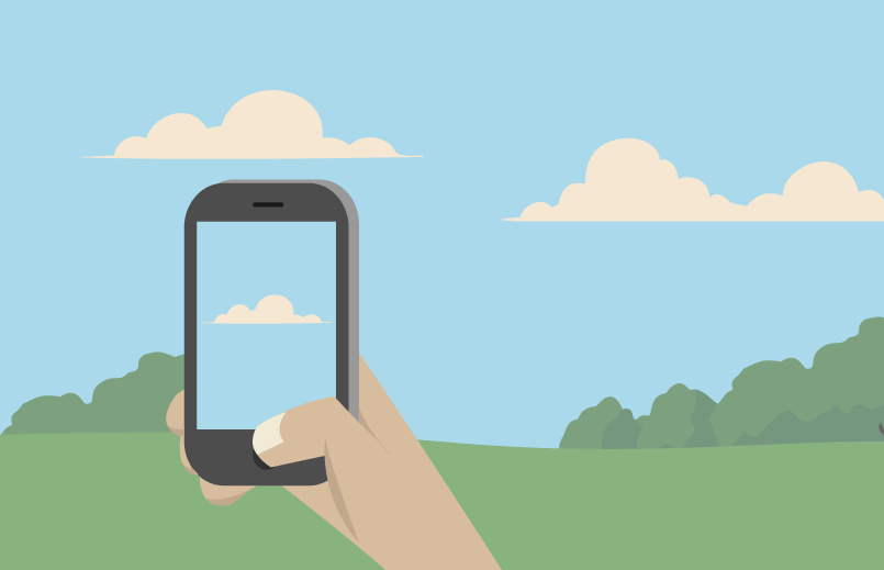 An illustration of a hand holding a rectangular smartphone and taking a picture of a cloud. The hand is beige colored with a lighter tan thumb nail shown. The hand is positioned like it is holding a phone with most of the fingers covered by the phone and only the thumb fully visible. The thumb is pushing a button at the bottom of the phone. The phone is black and gray with a rectangular screen. On the screen is a picture of a blue sky and a white cloud. The background has a blue sky with two white puffy clouds at the top and a green ground at the bottom. At the top of the green ground are green puffy bushes that look like the top of trees from a distance.