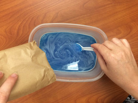 photo of blue gelatin powder being poured into a clear bowl of water